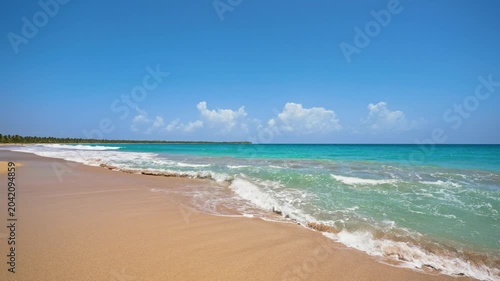 An exotic beach with golden sand, turquoise ocean water, and a blue sky with clouds on a sunny day. Wide panoramic seascape concept. Amazing landscape of the paradise coast. Waves on the sand.