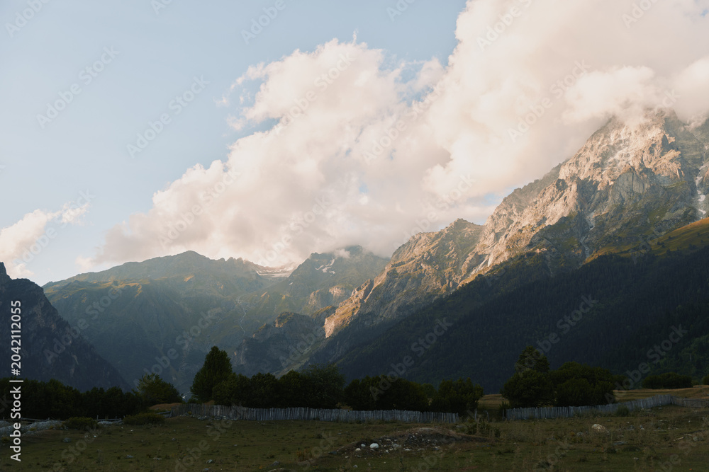Fototapeta premium Tranquil mountain landscape with rugged peaks, blue sky and fluffy clouds. A vast valley below conveys outdoor exploration, nature appreciation, and serene travel vibes.