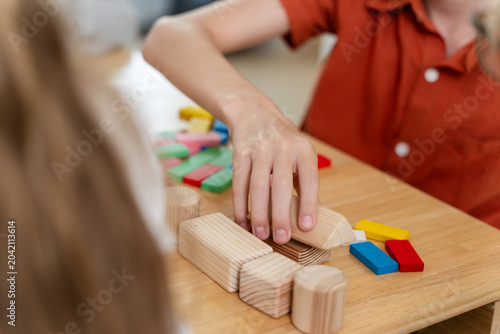 Primary teacher guides block pattern activity at wooden desk, arranging natural learning material while young pupil observes, supporting classroom routine, instruction, and early math understanding