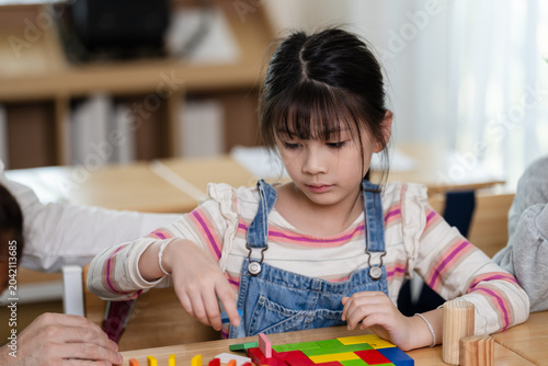Canvastavla Asian elementary girl places colorful block during teacher guided desk activity,