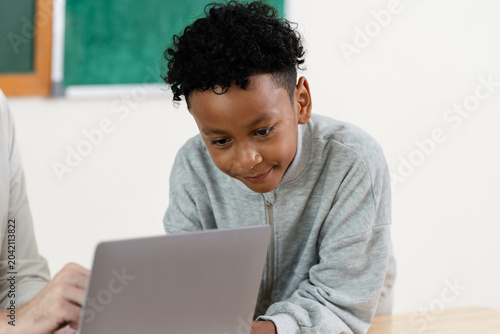 Konstfotografi Elementary boy smiles while using laptop during teacher supported classroom task