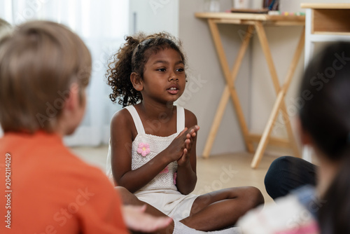 Young girl claps while speaking in classroom circle with peer group, practicing participation, encouragement, listening, confidence, and positive discipline during first day school activity today