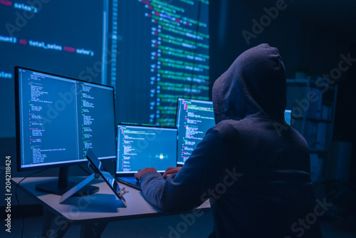 Hacker analyzing code in a dark room with multiple monitors technology environment cybersecurity concept