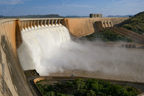 A powerful cascade of water flows over a massive dam during a summer afternoon