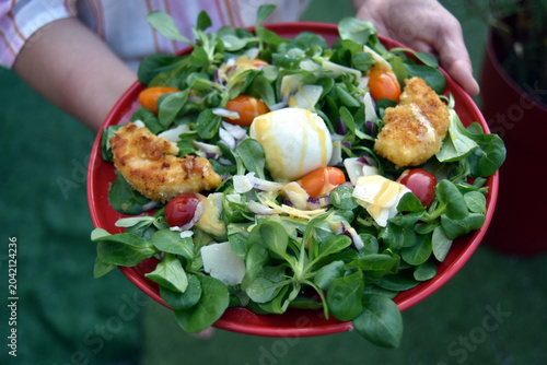 closeup of mixed salad in a red plate in hands of woman