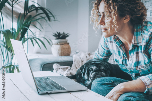 Fotografía Woman working on laptop at home with her pug on the couch, remote work in a cozy