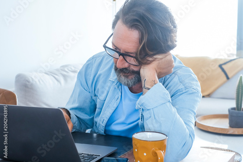 Εκτύπωση καμβά Middle-aged man working on a laptop at home, looking thoughtful while leaning on