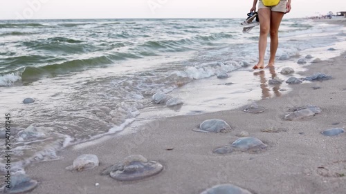 A girl with tanned legs walks along the beach that was strewn with dead dangerous jellyfish
