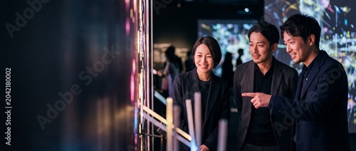 Asian business people digital art exhibition looking at glowing neon light interactive installation in a modern futuristic museum gallery experiencing technology innovation and creative inspirations.
