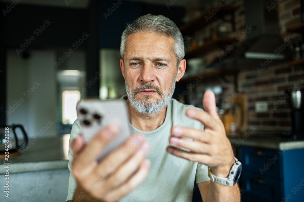 Φωτογραφία Middle-aged man troubleshooting smartphone at home kitchen