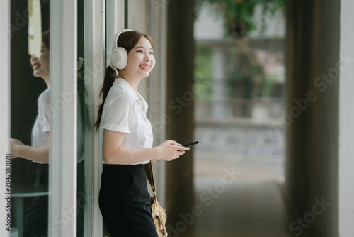 Obraz na płótnie Smiling young Asian woman listening to music with wireless headphones, holding a