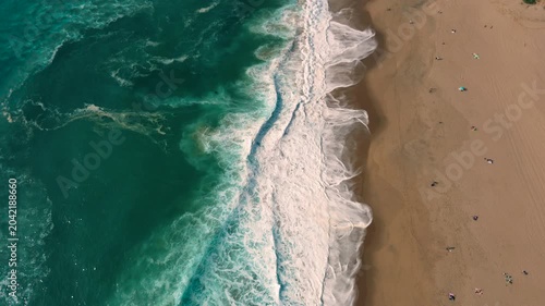 Aerial shot of the ocean with blue colours, waves doing  patters, rocks, sand and beach. Beautiful scenery