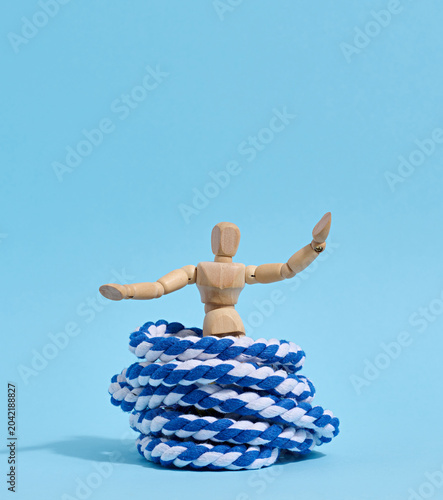 A wooden mannequin with raised arms is released from a trap shaped like a skein of blue and white rope a