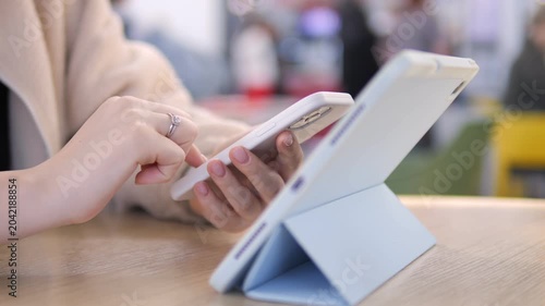 Person uses tablet on wooden table in cafe. Hands tap screen with focus. Background blurred with warm tones. Suitable for digital lifestyle, work-from-anywhere, or tech-related content