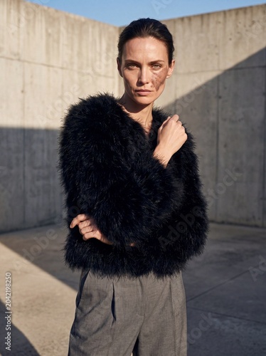 High fashion outdoor portrait of woman in black faux fur jacket and tailored trousers for editorial lookbook and seasonal campaign background