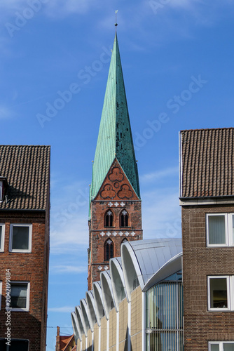 Fotografie A tall church spire reaches for the bright blue sky above Lübeck