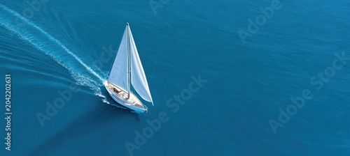 A solitary sailboat glides across vast, deep blue waters, leaving a white wake