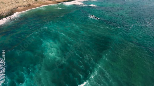 Aerial shot of the ocean with blue colours, waves doing  patters, rocks, sand and beach. Beautiful scenery