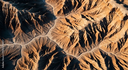 Top-down view of eroded desert hills with winding road, sunlit, arid terrain