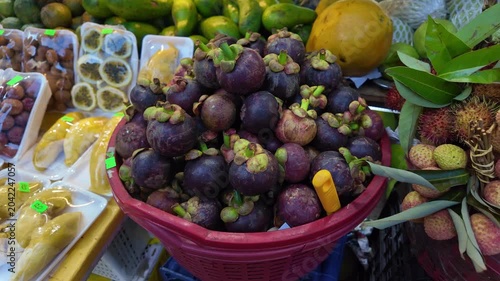 Close up view of fresh purple mangosteen in a red basket, surrounded by an assortment of exotic fruits like durian, rambutan, and passion fruit at a traditional vietnamese food market