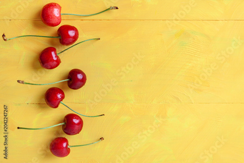 Fresh ripe red cherries with long stems arranged in a line on a yellow wooden table. sweet summer berry, organic food background