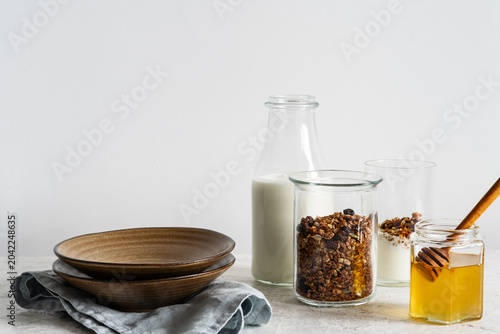Healthy granola breakfast on light background, homemade granola, yogurt, honey, and bottle of milk