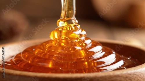 Thick golden honey pouring into a wooden bowl, close-up