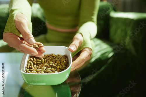 Close-up of a person in athletic wear holding a bowl of raw pumpkin seeds, highlighting a mindful and nutritious choice for clean eating.
