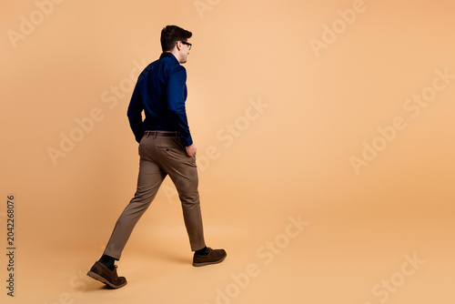 Fotografie Man walking away in business casual clothing on beige studio background showing