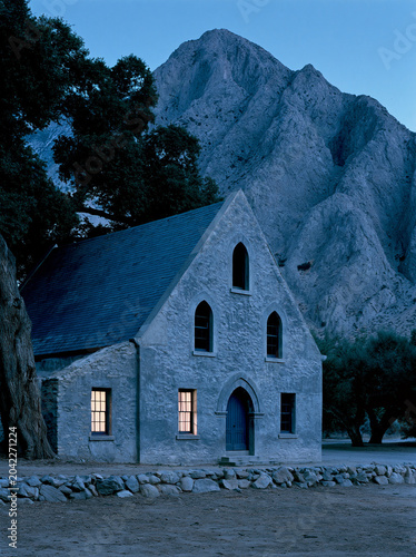 White countryside church beneath rocky mountain cliffs