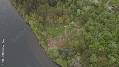  Aerial drone footage capturing the serene landscape of Stokka lake in Stavanger, Norway. The scene features a vast, calm body of water surrounded by lush greenery, captured at midday.