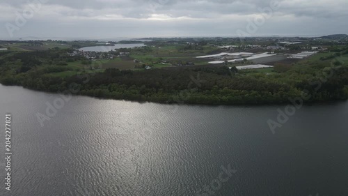  Aerial drone footage capturing the serene landscape of Stokka lake in Stavanger, Norway. The scene features a vast, calm body of water surrounded by lush greenery, captured at midday.