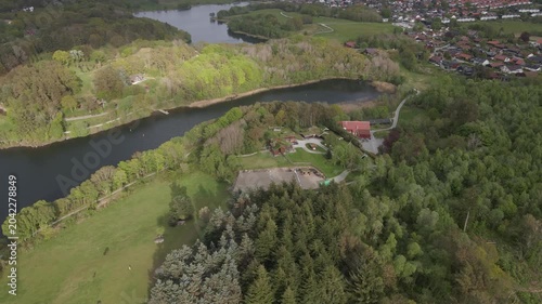  Aerial drone footage capturing the serene landscape of Stokka lake in Stavanger, Norway. The scene features a vast, calm body of water surrounded by lush greenery, captured at midday.