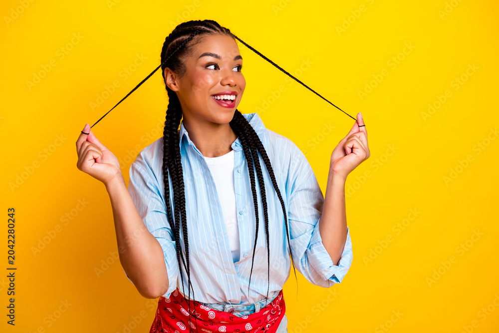 Naklejka premium Young woman with braids pulls hair ties against bright yellow background smiling for fashion lifestyle stock photo