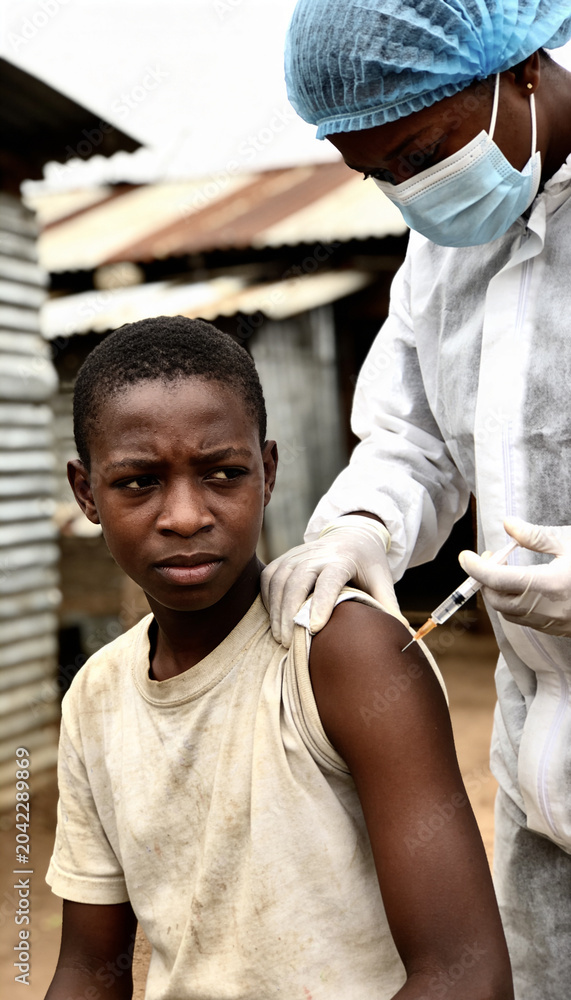 Fototapeta premium Woman doctor in protective suit administering vaccine to African teen boy in impoverished area. Medical help during virus pandemic. Vaccination campaign for children in rural setting.