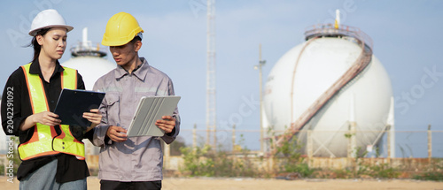 Asian Engineers Reviewing Data on Tablet and Clipboard at Industrial Gas Storage Facility