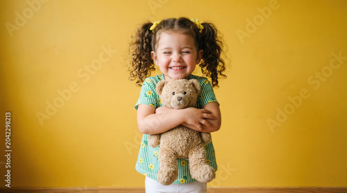 Joyful toddler hugging teddy bear against bright yellow wall