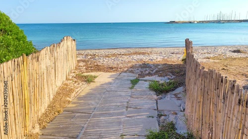 First person POV walk from a sandy path leading to the sea. Immersive coastal transition with beach scenery, blue water and summer travel atmosphere.
