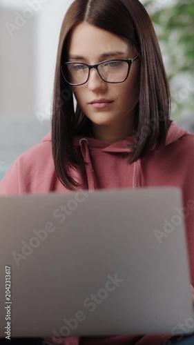 A woman sits on a couch using a laptop while studying in a cozy space at home.