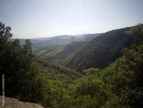 Obraz na plátne valle verde tra due colline boscose, con vegetazione fitta in primo piano e ciel