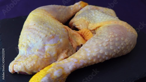 Two raw chicken legs are resting on a black board