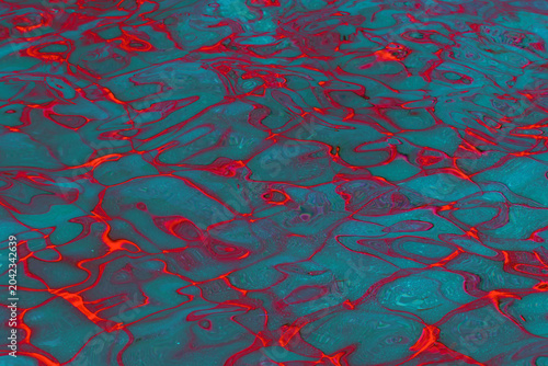 Abstract teal and red water reflections with rippling pattern and vibrant flu...