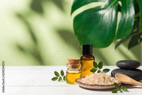 Beauty treatment items for spa procedures on white wooden table. massage stones, essential oils and sea salt. Light green background both a green plant. copy space