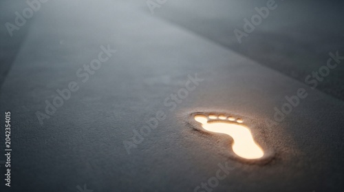A single glowing footprint illuminates a mysterious dark path, symbolizing guidance, progress, and the start of a new journey into the unknown future