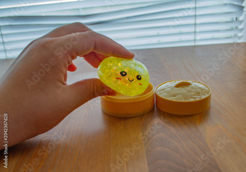 Obraz na płótnie Close-up: a person's hand reaches for a yellow shiny squishy with a cute face over an open steamer container
