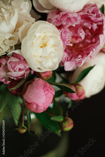 Mixed peony bouquet with white and deep pink blooms and pink buds against a dark background, warm light, close-up floral composition