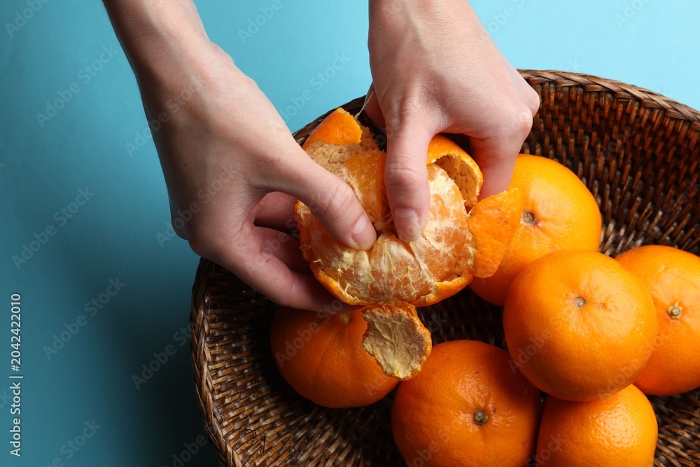 Obraz premium Woman peeling ripe tangerine and fresh fruits on light blue background, top view