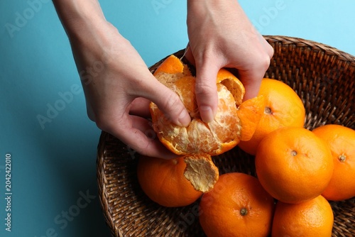 Woman peeling ripe tangerine and fresh fruits on light blue background  top view