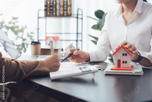 Foto Real Estate Deal in Progress: Two individuals, a potential buyer and a real estate agent, engage in a discussion about a property deal, symbolized by a miniature house model and signed documents