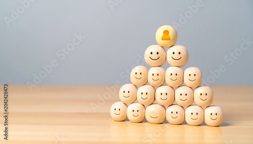 Pyramid of wooden spheres with smiley faces and one yellow sphere with a person icon at the top on a light wooden surface, symbolizing leadership, positivity, and teamwork.